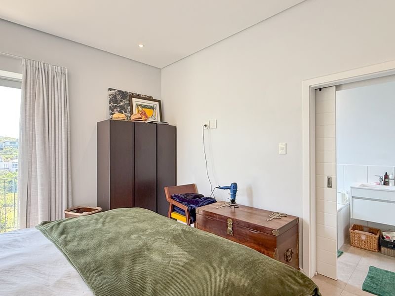 A well-lit bedroom featuring neutral walls, a large window with natural light, and direct access to an en-suite bathroom via a sliding door.