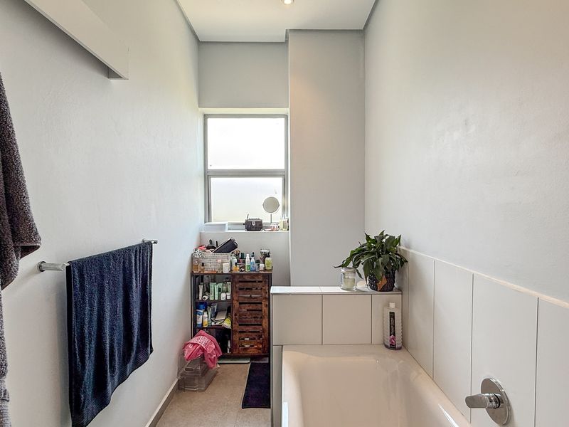A functional bathroom featuring a built-in bathtub with tiled splashback and a window providing natural light.