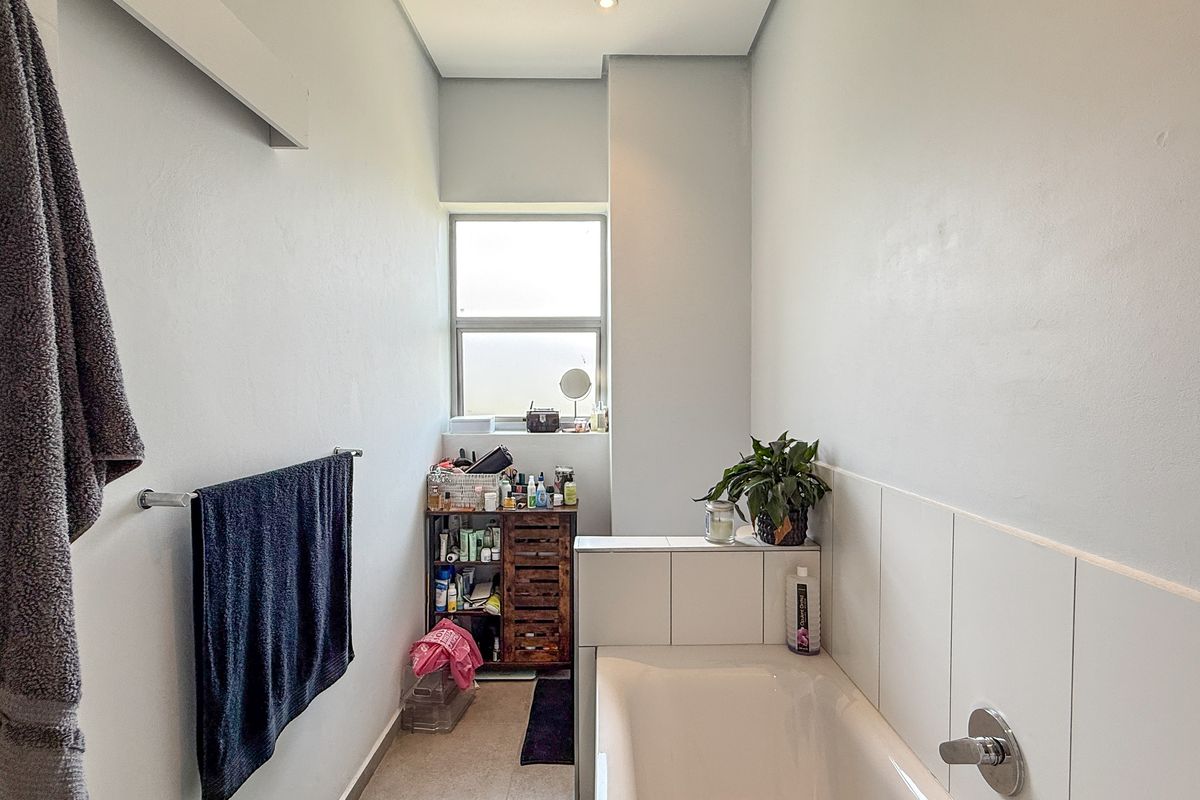 A functional bathroom featuring a built-in bathtub with tiled splashback and a window providing natural light.