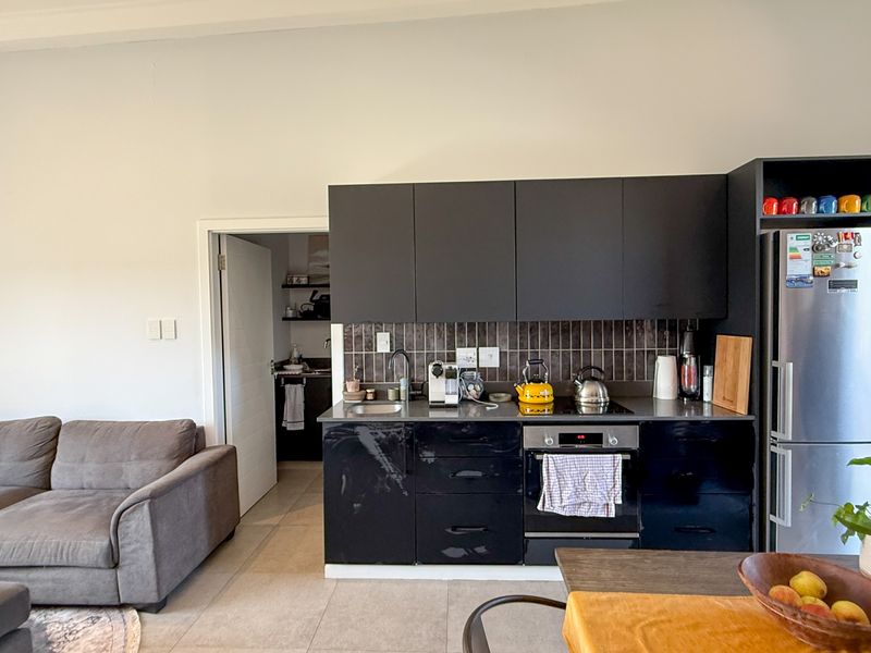 Open-plan living area featuring a modern kitchen with dark cabinetry, integrated oven, hob, and tiled backsplash, seamlessly connected to the lounge space.