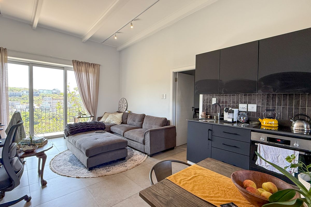 Modern open-plan living area featuring a sleek kitchen with dark cabinetry, integrated oven, and direct access to a balcony with scenic views.
