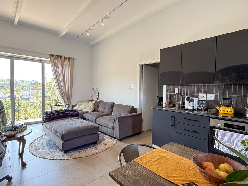 Modern open-plan living area featuring a sleek kitchen with dark cabinetry, integrated oven, and direct access to a balcony with scenic views.