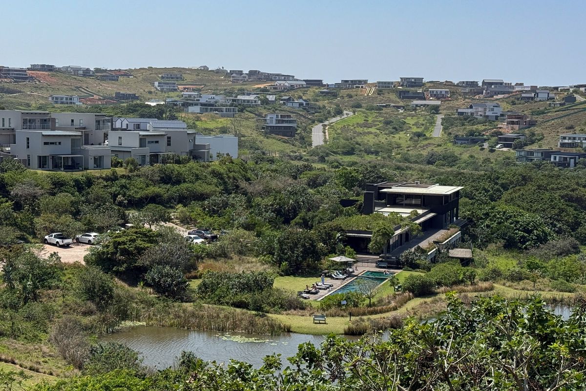 An elevated aerial view of a modern residential estate featuring a swimming pool, natural pond, and surrounding landscaped greenery.