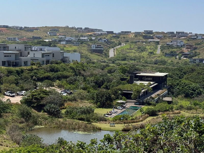 An elevated aerial view of a modern residential estate featuring a swimming pool, natural pond, and surrounding landscaped greenery.