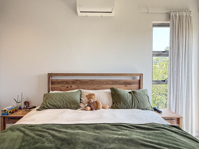 A well-maintained bedroom featuring a built-in wardrobe, split-system air conditioning, and direct access to an outdoor area through a sliding glass door.