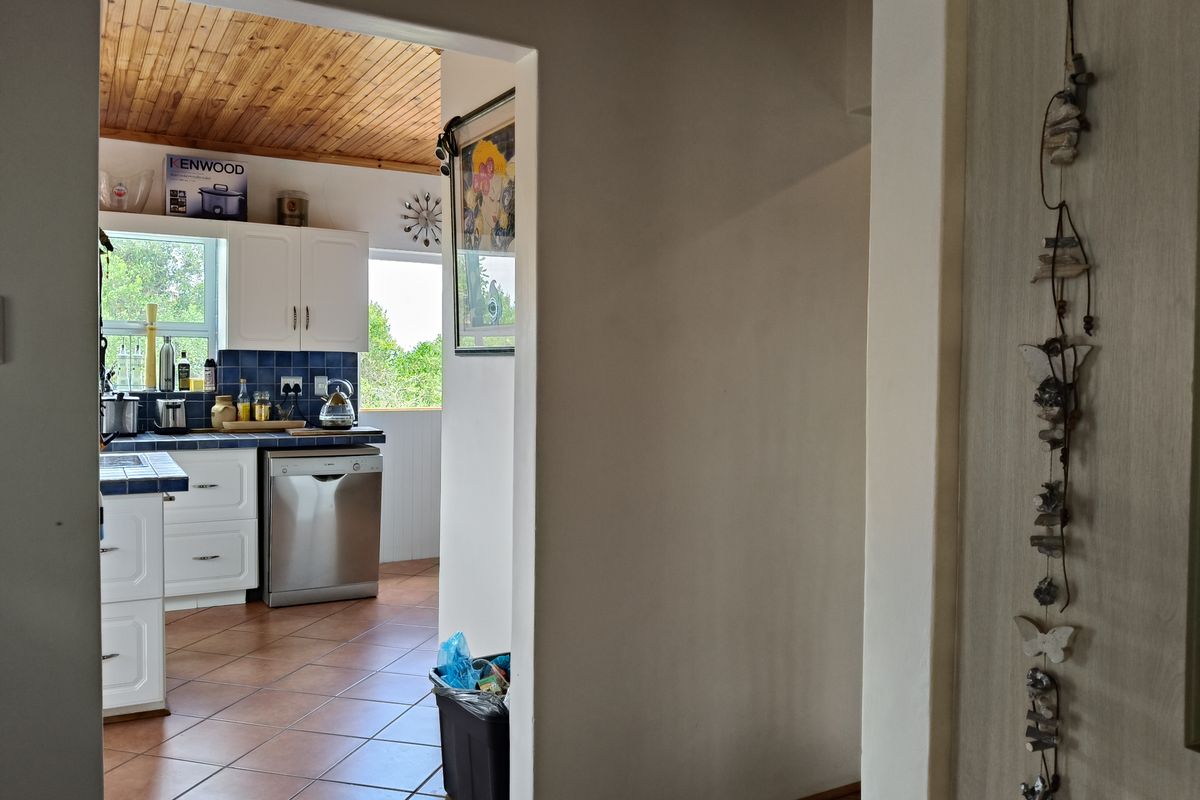 A view from a hallway into a kitchen featuring white cabinetry, blue tiled countertops, a timber-clad ceiling, and tiled flooring.