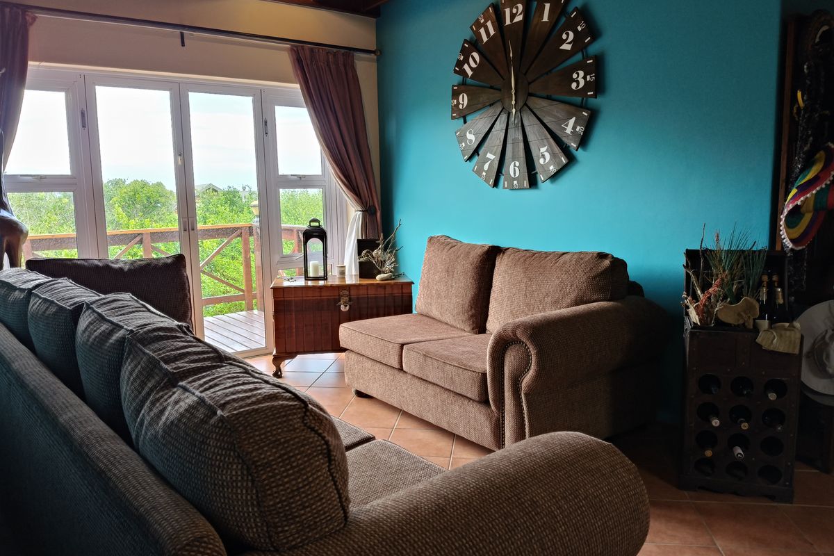 A comfortable living room featuring tiled flooring, exposed timber ceiling beams, and large glass sliding doors providing access to an outdoor balcony.