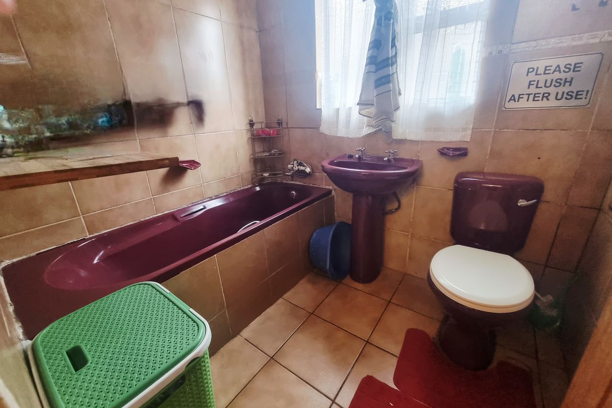 A dated bathroom featuring a burgundy bathtub, pedestal basin, and matching toilet, finished with beige wall and floor tiling.