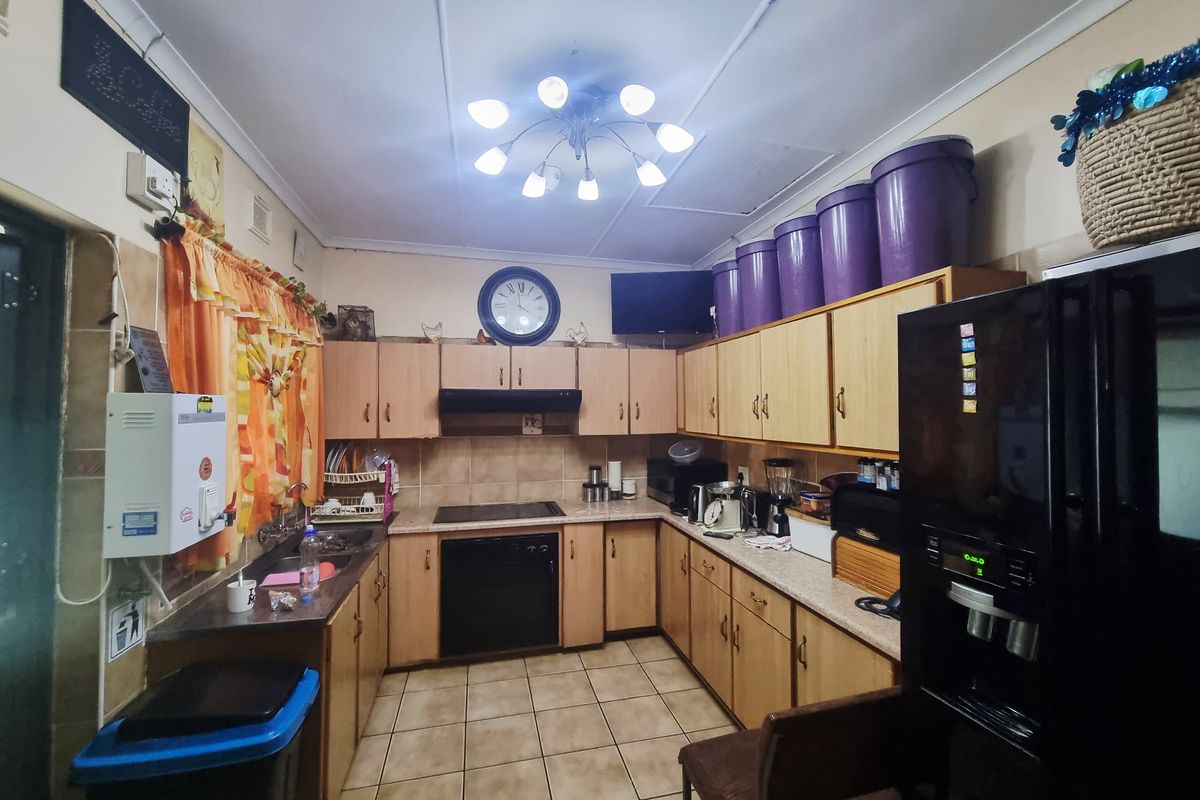 A functional kitchen featuring U-shaped wooden cabinetry, integrated hob and oven, tiled splashbacks, and tiled flooring with ample storage space.