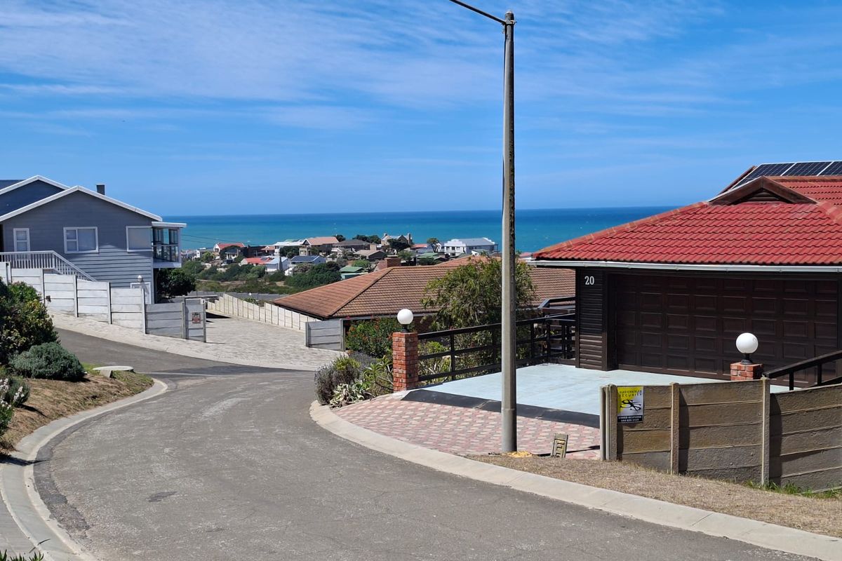 A street-level view of a residential neighborhood featuring paved roads, established homes with tiled roofs, and a distant ocean view.