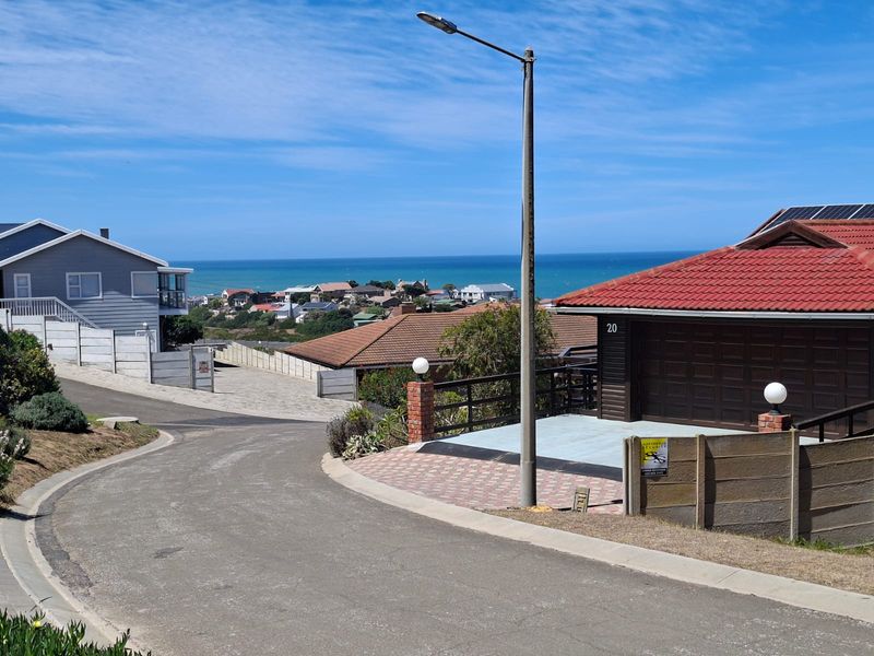 A street-level view of a residential neighborhood featuring paved roads, established homes with tiled roofs, and a distant ocean view.