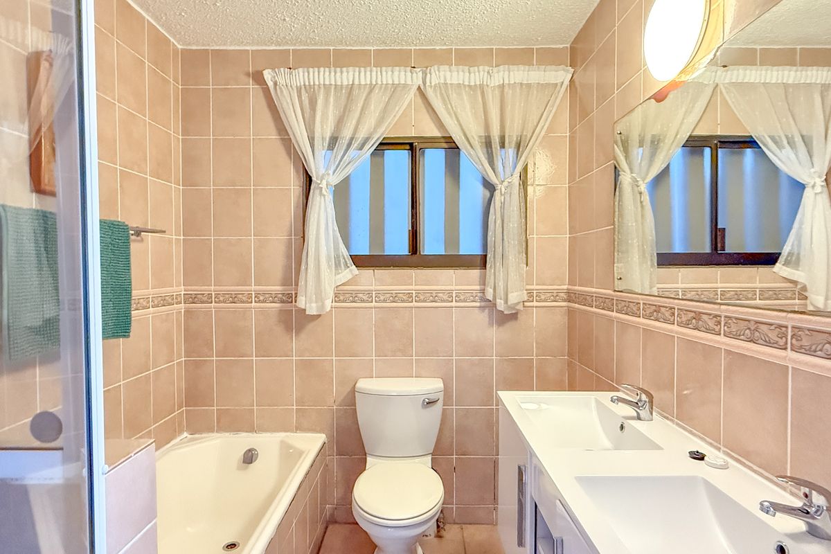A functional bathroom featuring a built-in bathtub, a dual-basin vanity unit, and full-height wall tiling.