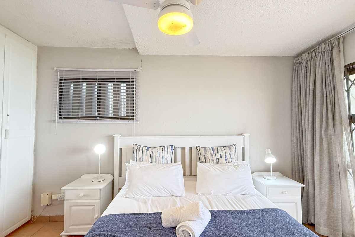 A bedroom featuring built-in wardrobes, a ceiling fan, and a window with blinds, providing a functional and comfortable sleeping space.
