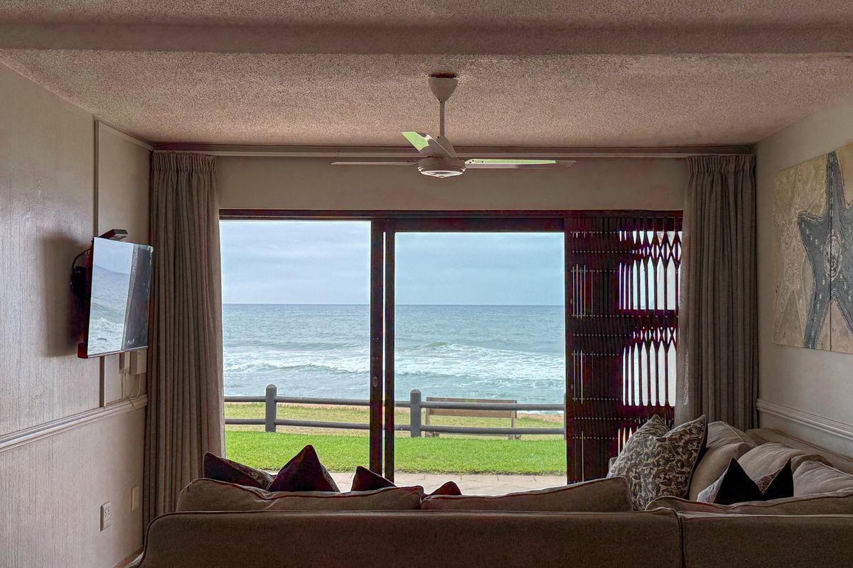A comfortable living room featuring large sliding glass doors that open to a scenic ocean view and a ceiling fan.