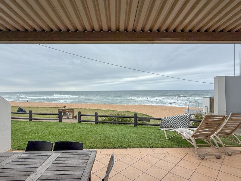 A covered patio area featuring tiled flooring and direct access to a lawn with unobstructed ocean and beach views.