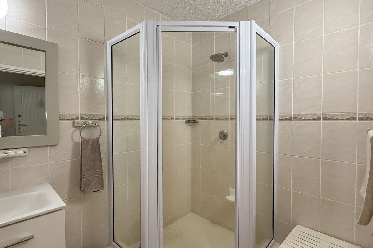A functional bathroom featuring a corner shower enclosure with white frame, a wall-mounted vanity basin, and neutral ceramic wall tiles.