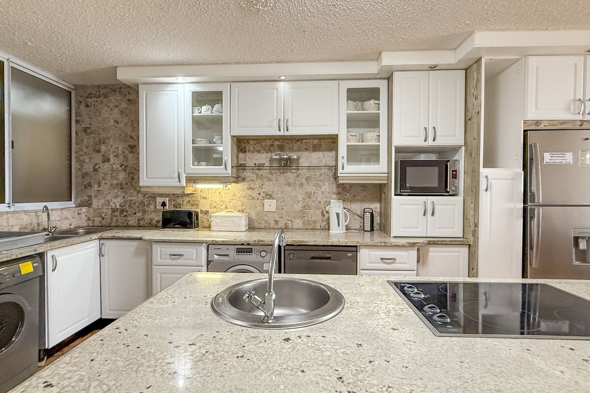 A functional kitchen featuring white cabinetry, granite countertops, a central island with a built-in hob and sink, and integrated appliance spaces.