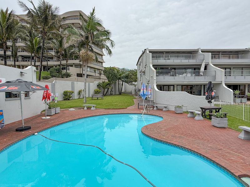 Communal swimming pool area featuring brick paving, landscaped garden space, and views of the apartment complex buildings.