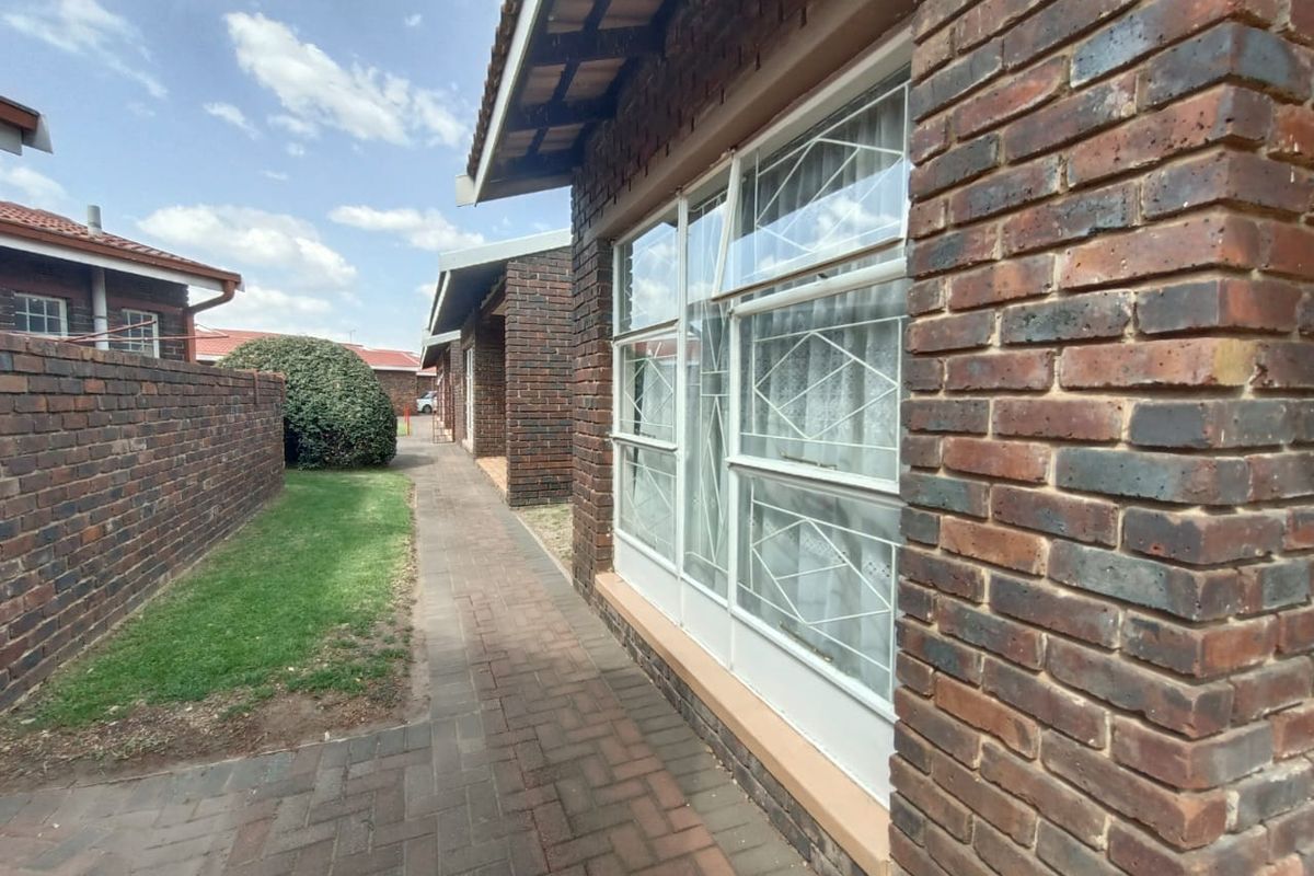Exterior view of the property featuring face-brick facade, paved walkway, and security-barred windows along the side elevation.