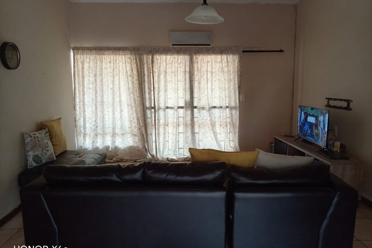 A living room featuring a wall-mounted air conditioning unit, large window with curtains, and tiled flooring.