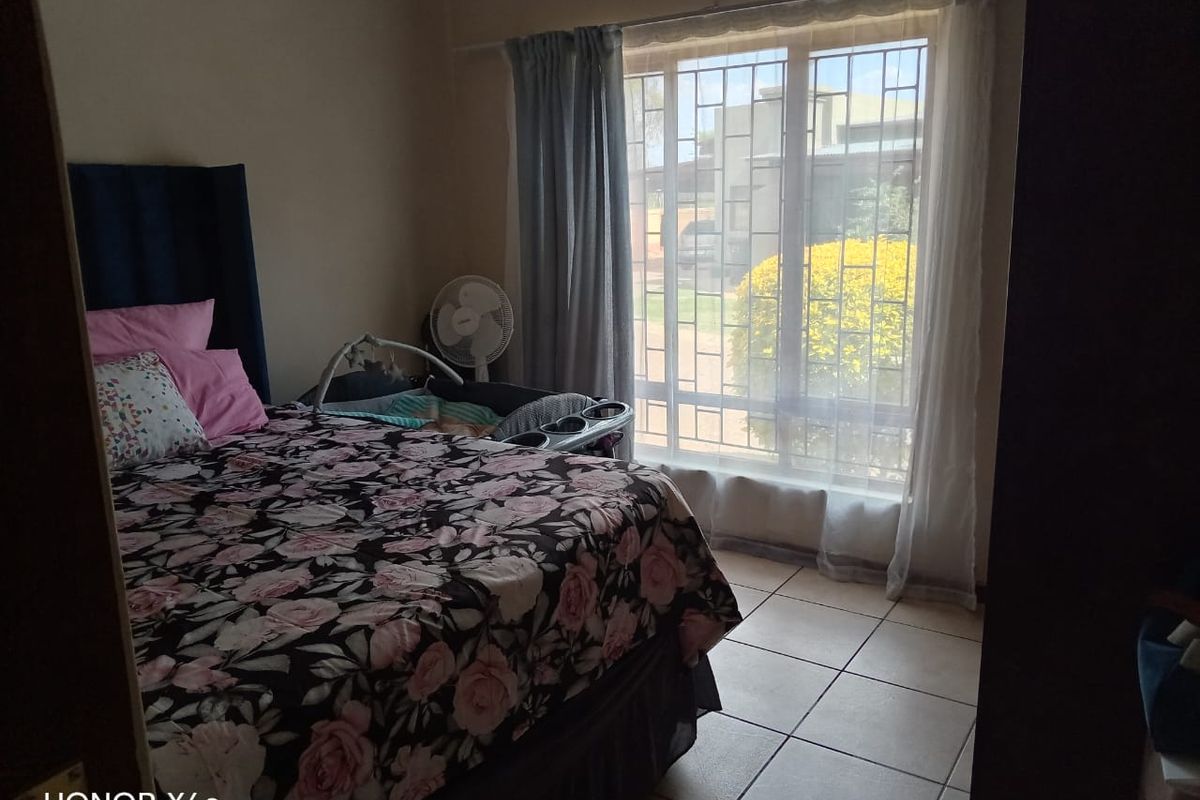 A bedroom featuring tiled flooring and a large window fitted with security bars, allowing natural light into the space.