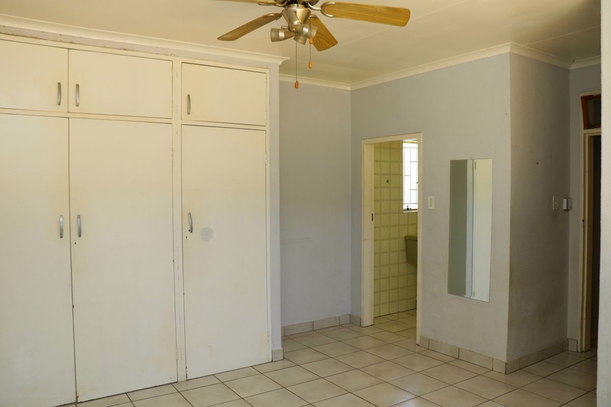 A bedroom featuring built-in floor-to-ceiling cupboards, tiled flooring, a ceiling fan, and direct access to an en-suite bathroom.