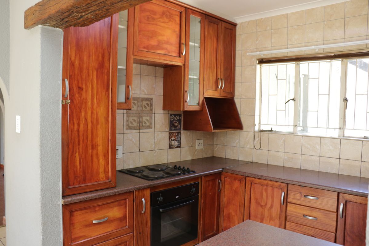 A functional kitchen featuring warm-toned wooden cabinetry, a built-in oven and hob, and a tiled backsplash with a window for natural light.