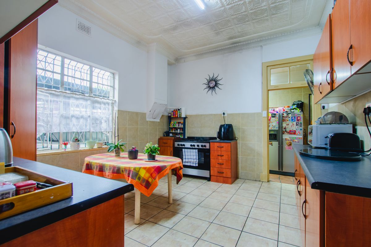 A functional kitchen featuring wooden cabinetry, tiled flooring, a built-in stove, and a decorative pressed ceiling, with an adjacent scullery area.