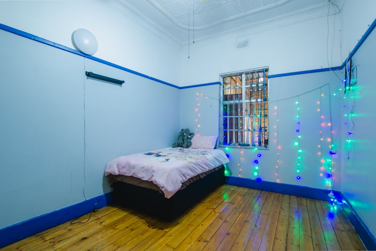 A bedroom featuring original timber flooring, decorative ceiling detail, and a window fitted with security bars.