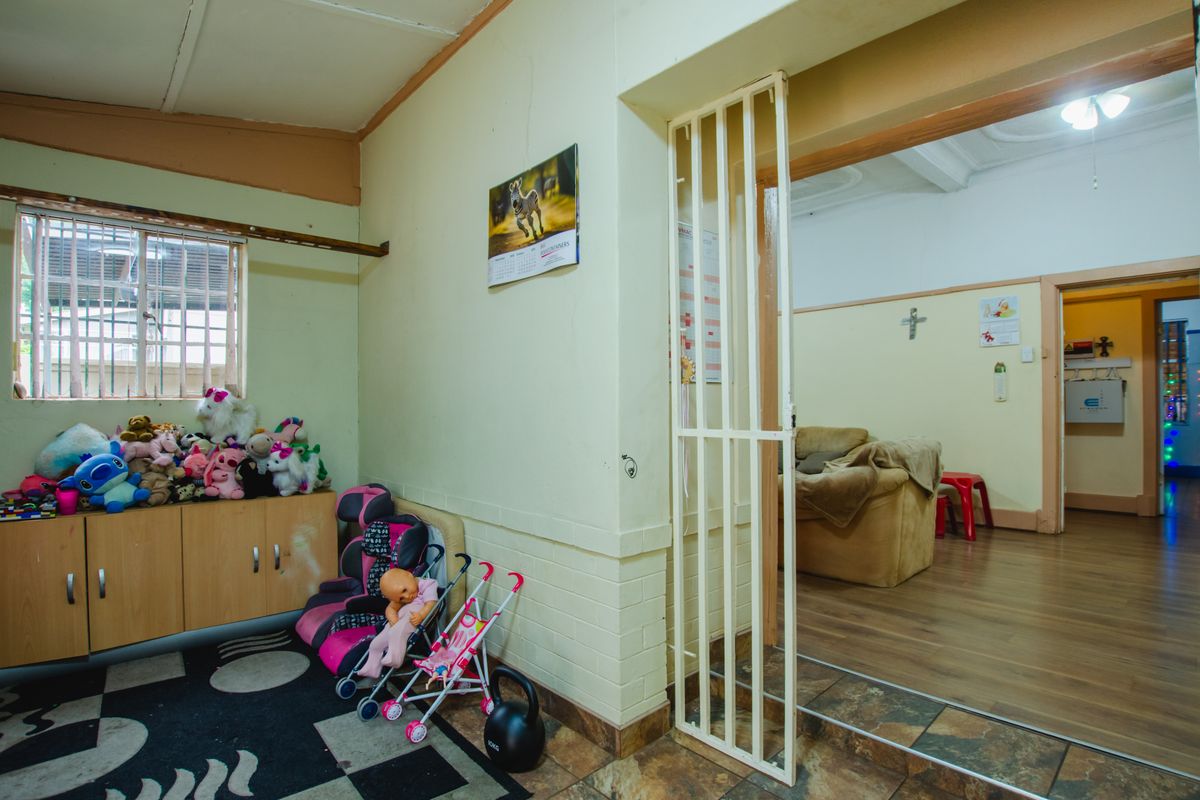 A multi-purpose living area featuring tiled flooring, a security gate partition, and access to an adjoining room with laminate flooring.