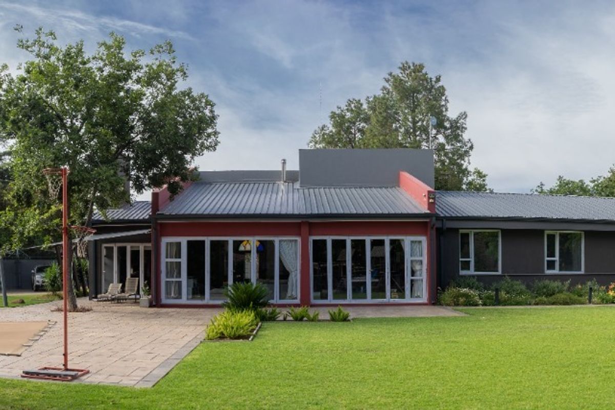 A spacious rear exterior view of the house featuring a large lawn, paved patio area, and extensive sliding glass doors leading into the home.