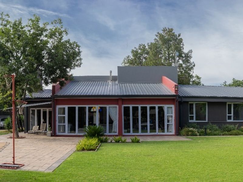 A spacious rear exterior view of the house featuring a large lawn, paved patio area, and extensive sliding glass doors leading into the home.