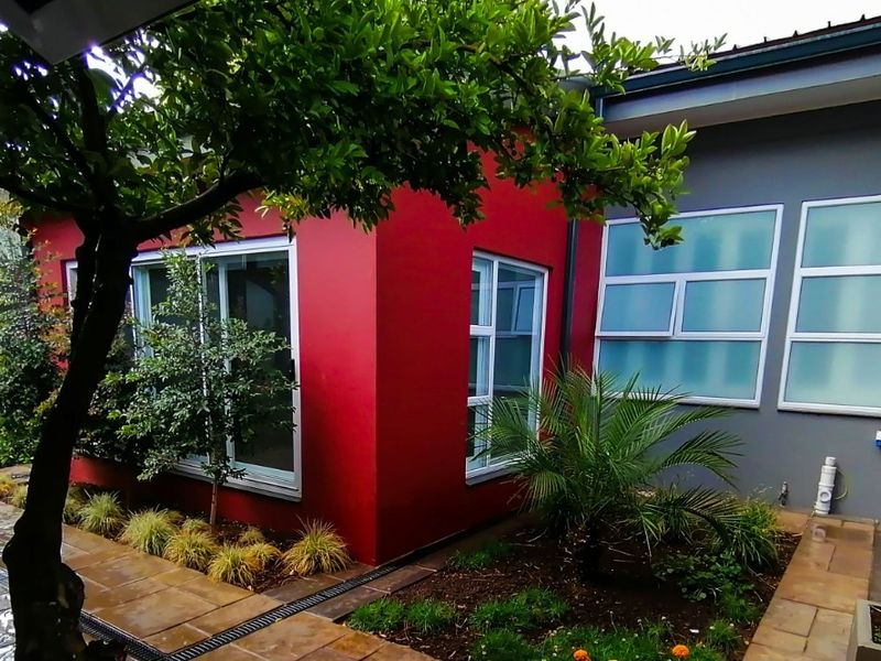 A well-maintained rear exterior view featuring a paved patio, landscaped garden beds, and modern sliding glass doors against a vibrant red and grey facade.
