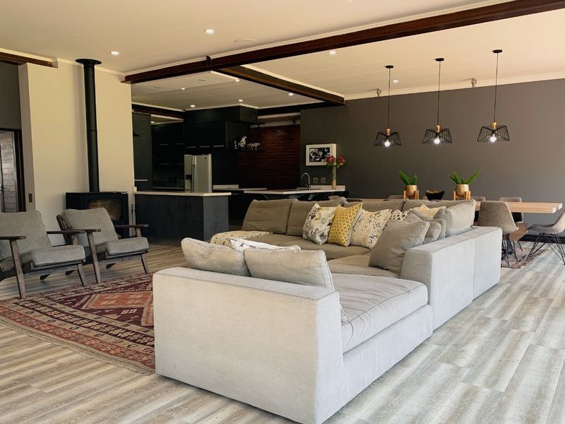 Spacious open-plan living area featuring a wood-burning fireplace, exposed structural beams, modern kitchen island, and contemporary pendant lighting throughout the dining and kitchen space.
