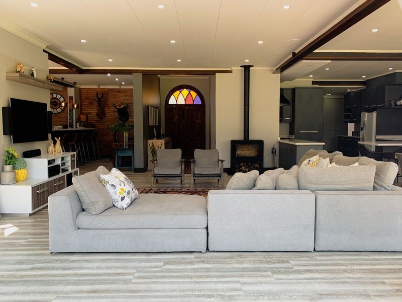 Spacious open-plan living area featuring a wood-burning fireplace, exposed timber beams, and a striking stained glass entrance door, seamlessly connecting to the kitchen.
