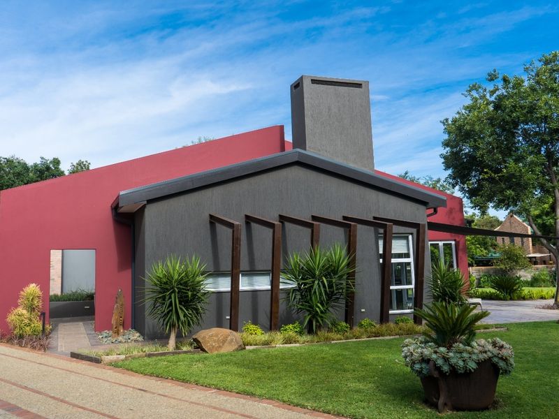 Modern architectural home exterior featuring a striking red and charcoal facade, prominent chimney, and well-maintained landscaped garden with paved driveway access.
