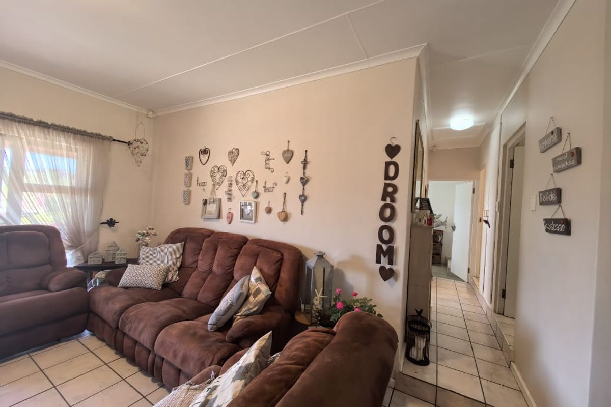 A comfortable living room featuring tiled flooring and a neutral color palette, providing access to the adjacent hallway and interior spaces.