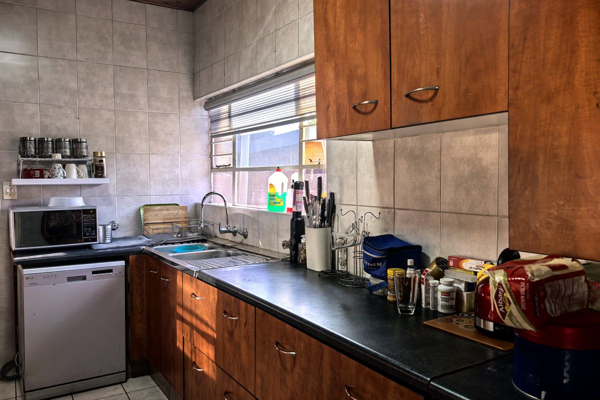 A functional kitchen featuring wood-veneer cabinetry, dark laminate countertops, a stainless steel sink, and tiled wall finishes.