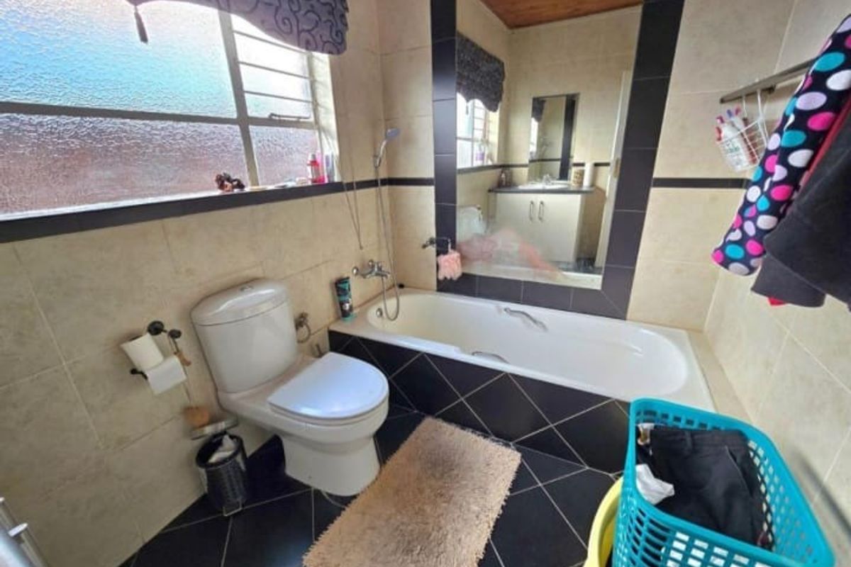 A functional bathroom featuring a built-in bathtub, toilet, and vanity mirror with tiled walls and flooring.