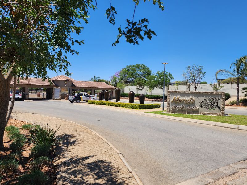 The entrance to Marula Heights Estate featuring a secure gatehouse, paved driveway, and well-maintained landscaped gardens with estate signage.
