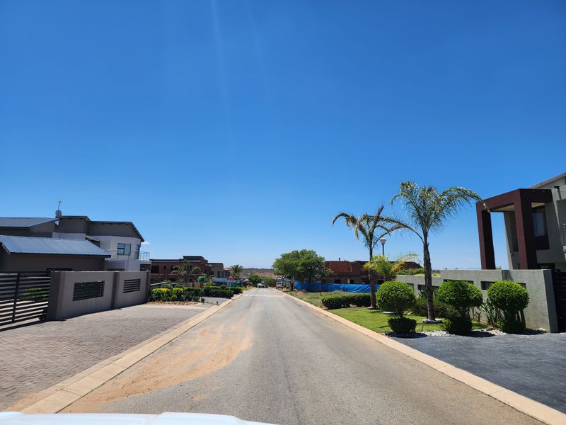 A clear street view of a modern residential estate featuring paved driveways, manicured landscaping, and well-maintained boundary walls under a clear blue sky.