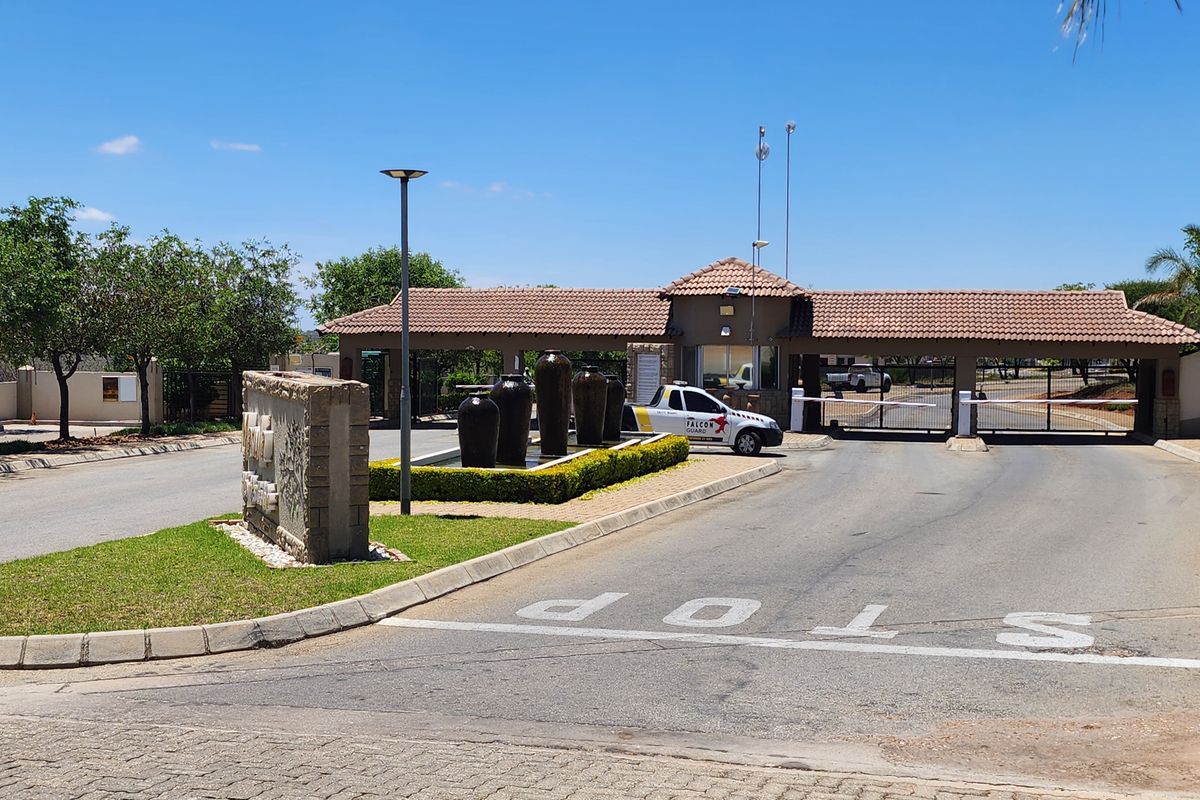 The entrance to the residential estate features a secure gatehouse, boom gate access, a paved driveway, and a landscaped water feature.