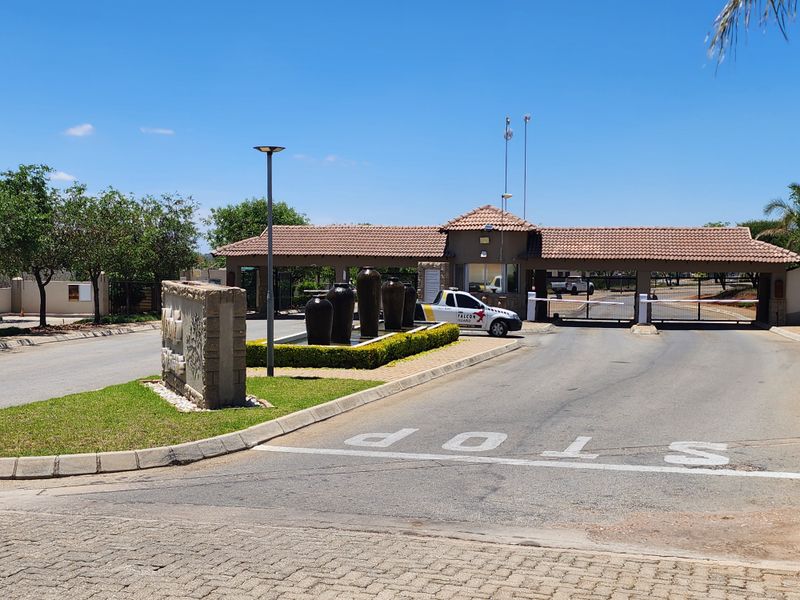 The entrance to the residential estate features a secure gatehouse, boom gate access, a paved driveway, and a landscaped water feature.