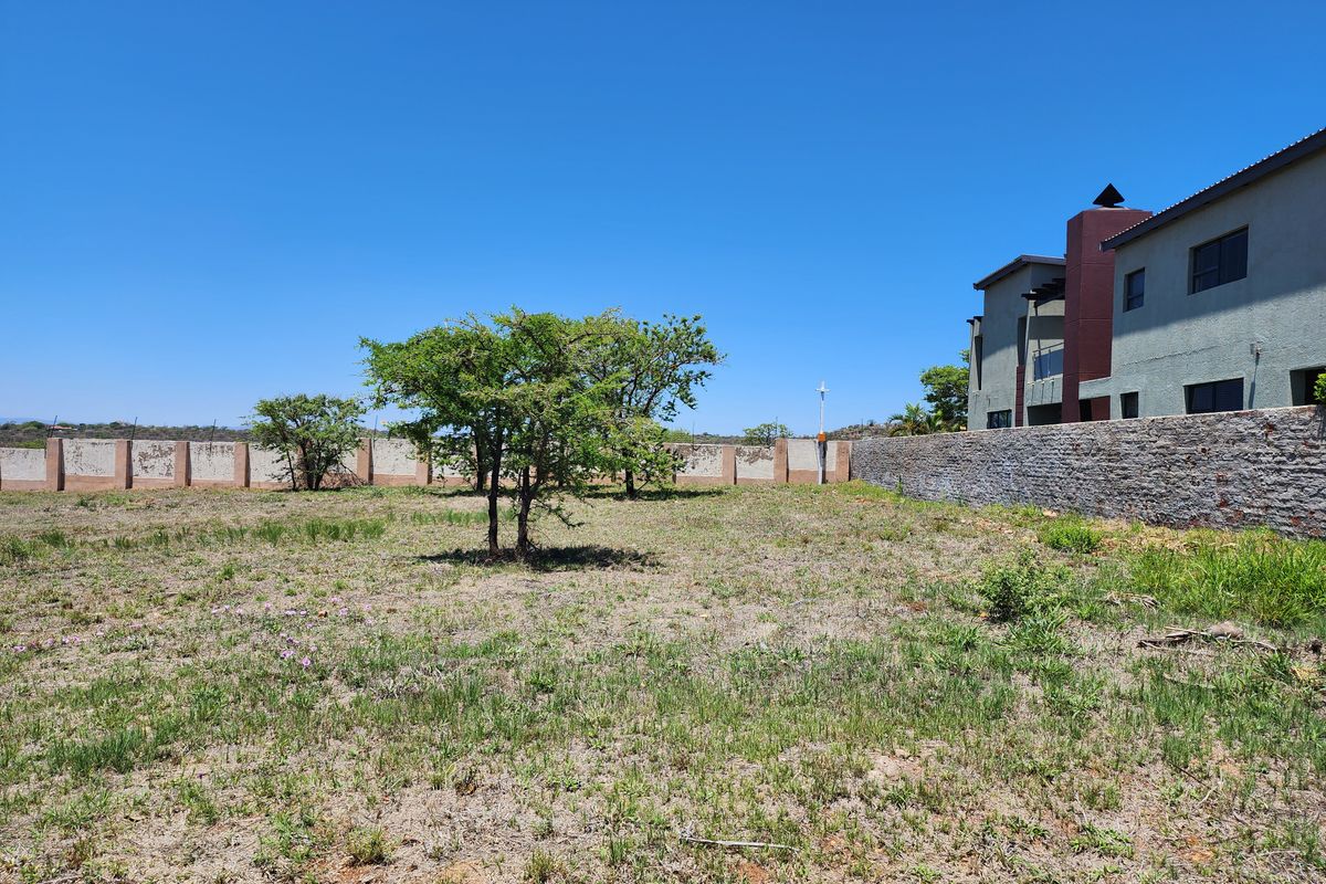 A view of the vacant residential land featuring a stone-clad boundary wall and established trees, adjacent to an existing multi-story residential structure.