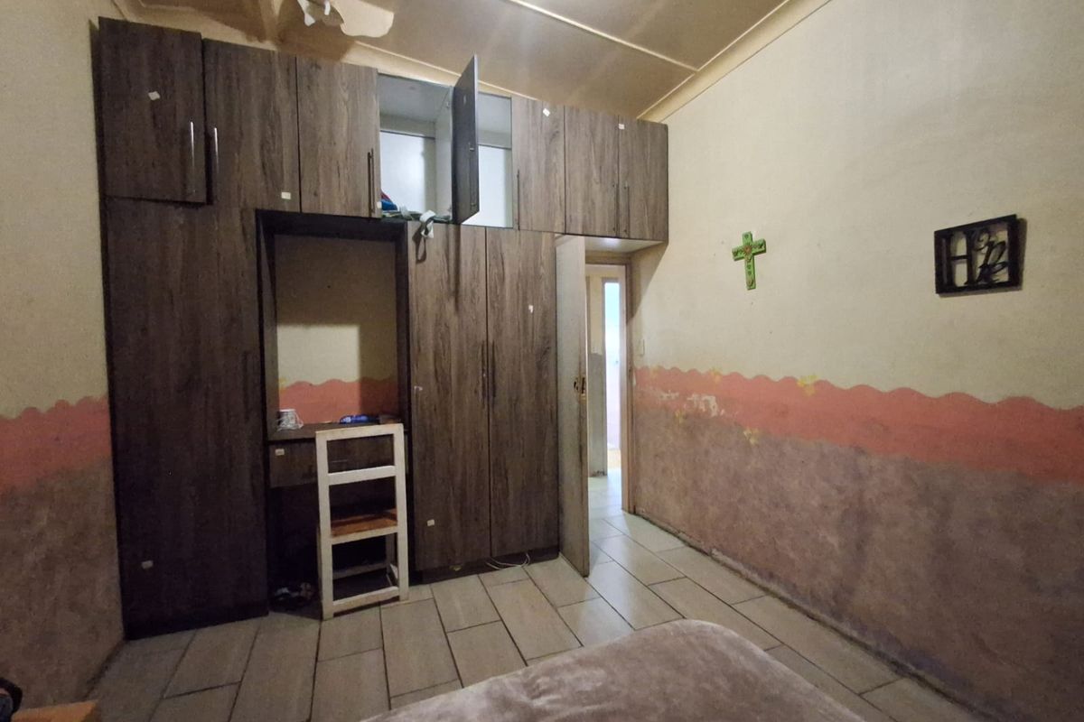 A bedroom featuring built-in wooden cabinetry, tiled flooring, and walls requiring cosmetic attention and repair.