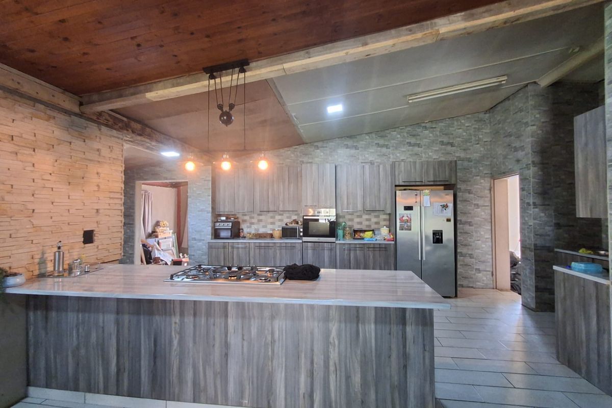 Modern open-plan kitchen featuring a large central island with a built-in gas hob, stone-cladding feature walls, and wood-paneled vaulted ceilings.