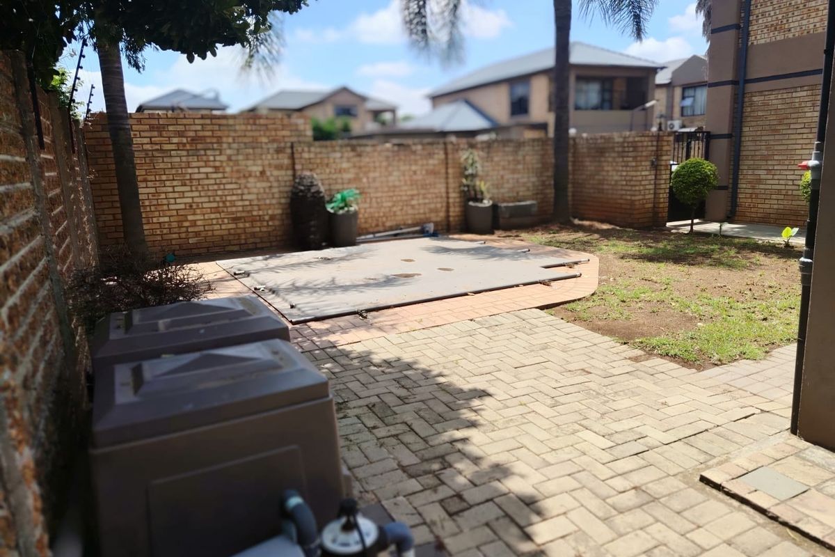 A private rear garden featuring a paved patio area, a swimming pool with a safety cover, and perimeter brick walling.
