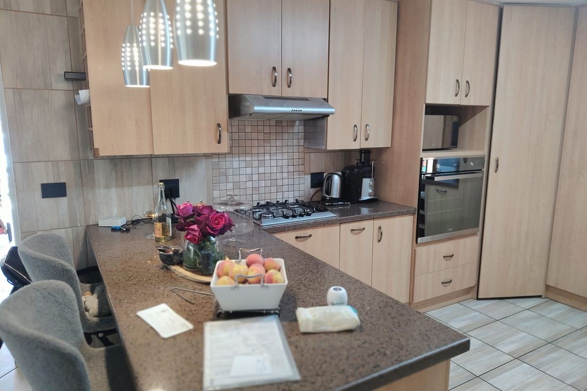 A functional kitchen featuring light wood cabinetry, a dark stone breakfast bar, built-in oven, gas hob, and tiled backsplash.