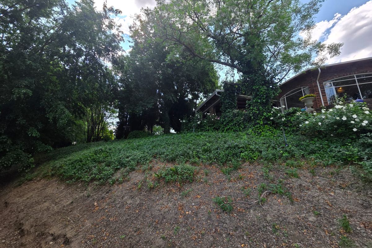 A view of the property's rear exterior, featuring a sloped garden area with mature trees and established greenery adjacent to the brick building structure.