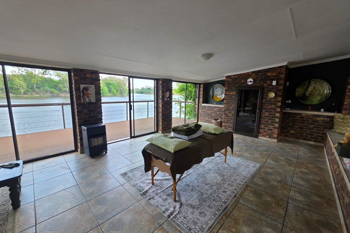 Spacious living area featuring exposed brick walls, tiled flooring, and large sliding glass doors opening onto a deck with scenic river views.